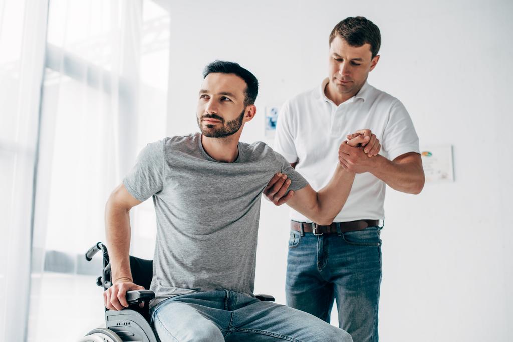 Fisioterapeuta ajudando o homem deficiente em cadeira de rodas durante a recuperação
 - Foto, Imagem