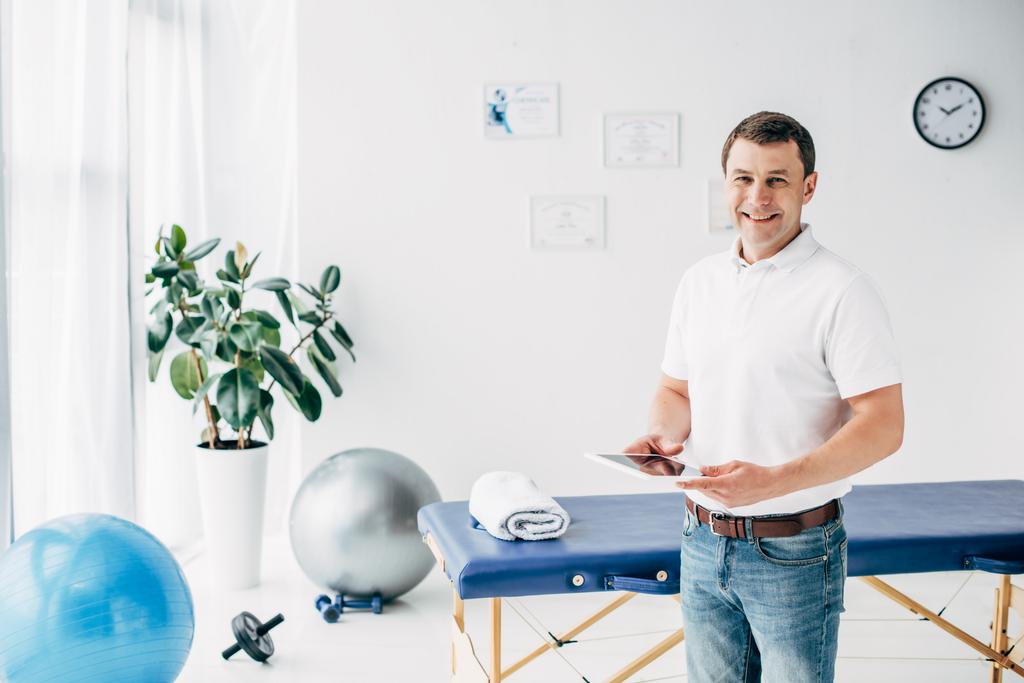 smiling chiropractor holding Digital Tablet in hospital and looking at camera - Photo, Image