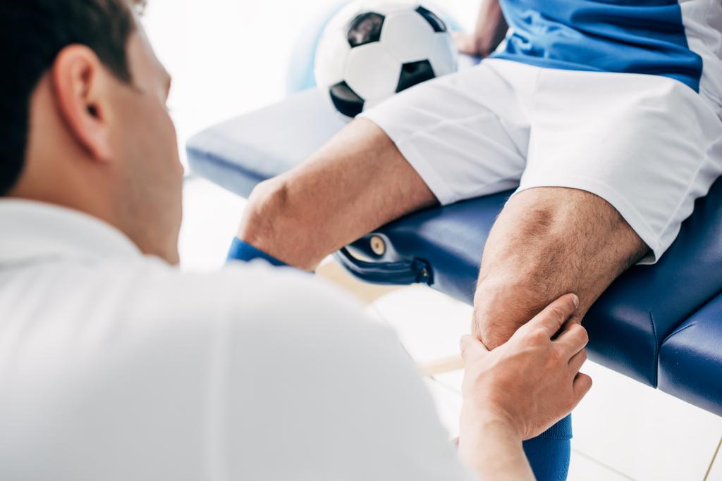 частичный взгляд физиотерапевта, массирующего ногу футболиста в больнице
 - Фото, изображение