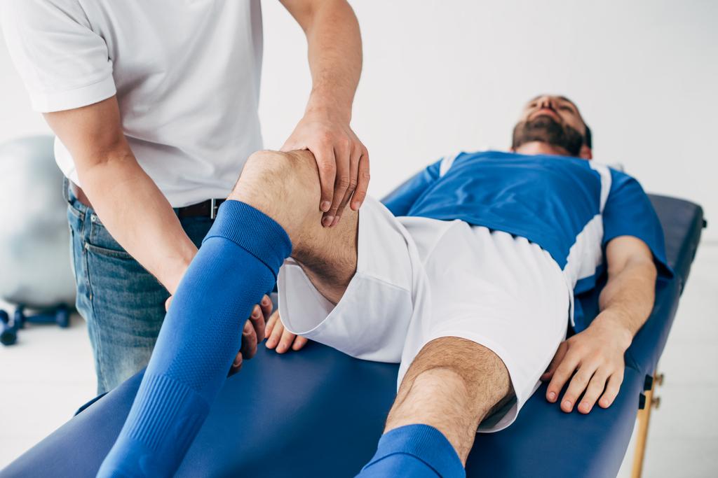 Φυσιοθεραπευτής μασάζ πόδι του παίκτη του ποδοσφαίρου στο νοσοκομείο - Φωτογραφία, εικόνα