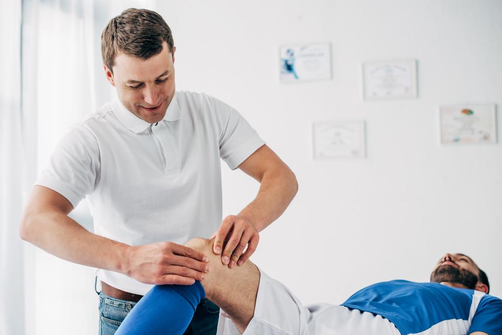 bonito fisioterapeuta massagem perna de jogador de futebol no hospital
 - Foto, Imagem