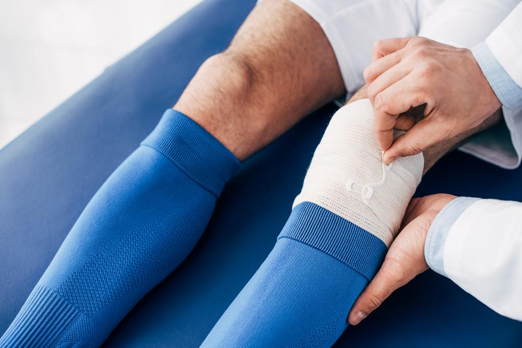 vista recortada de fisioterapeuta poniendo vendaje elástico en la pierna del jugador de fútbol
 - Foto, imagen