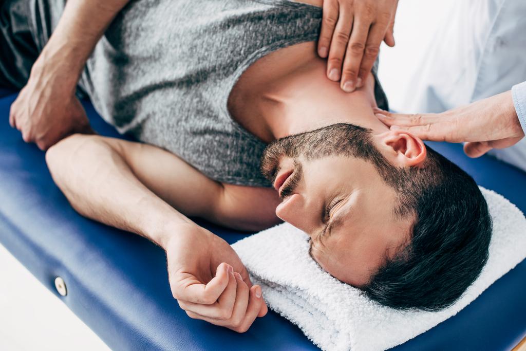 Chiropraktiker massiert Hals des auf Massagetisch liegenden Mannes - Foto, Bild