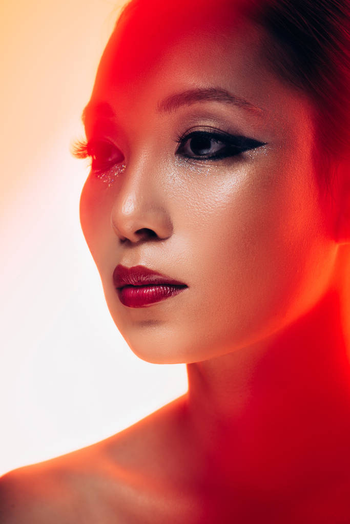 ελκυστικό ασιατικό κορίτσι με μακιγιάζ στο κόκκινο φως, τονισμένη εικόνα - Φωτογραφία, εικόνα