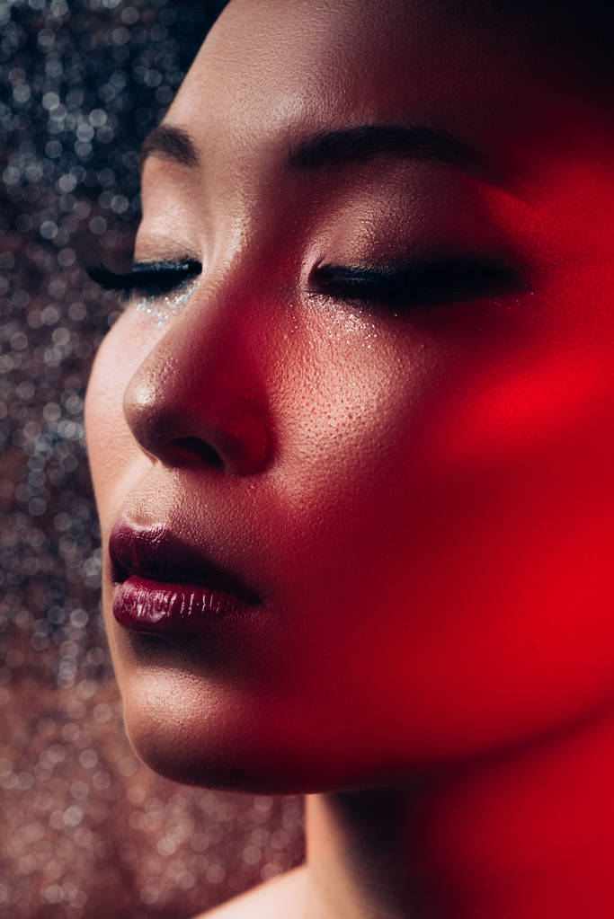 Nahaufnahme sinnlicher asiatischer Mädchen mit Make-up auf geschlossenen Augen im Rotlicht  - Foto, Bild