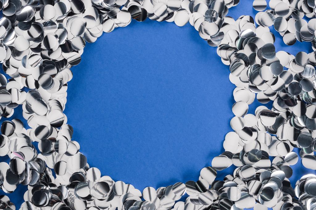 Top view of silver circle made of confetti on blue background  - Photo, Image