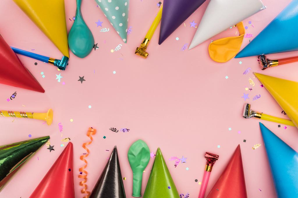 Вид сверху партийных рогов, шапок и конфетти на розовом фоне
 - Фото, изображение
