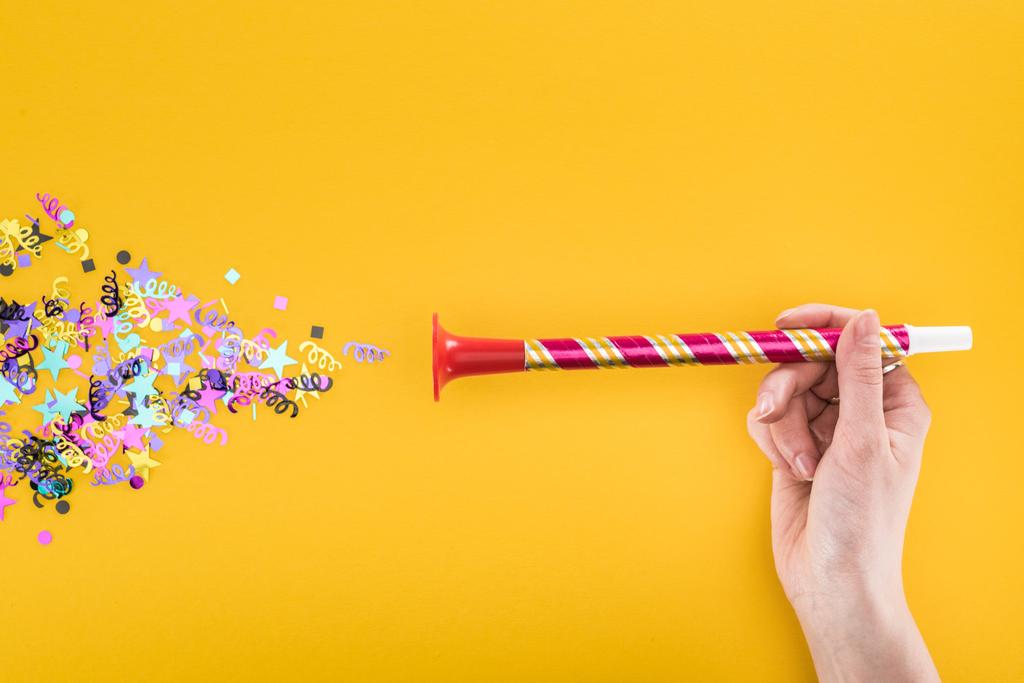 cropped view of woman holding party horn near confetti on yellow background - Photo, Image