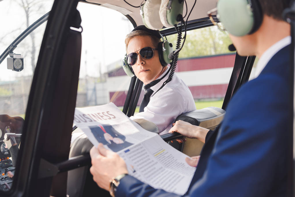 Proef in hoofdtelefoon en zakenman met krant in helikopter cabine - Foto, afbeelding
