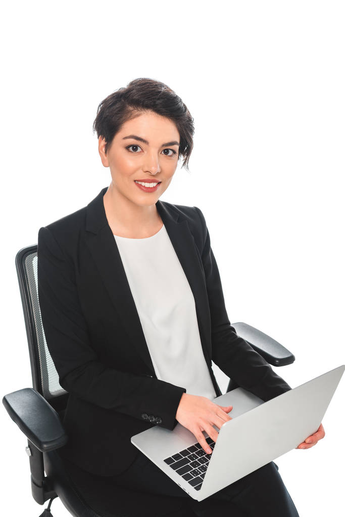 uśmiechnięta kobieta businesswoman przy użyciu laptopa siedząc w krzesło biurowe i patrząc na aparat na białym tle - Zdjęcie, obraz
