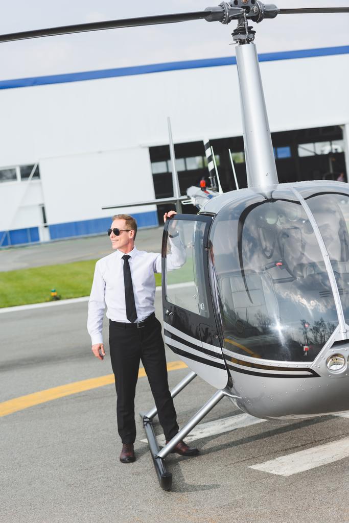 good-looking smiling Pilot in formal wear and sunglasses near helicopter - Photo, Image