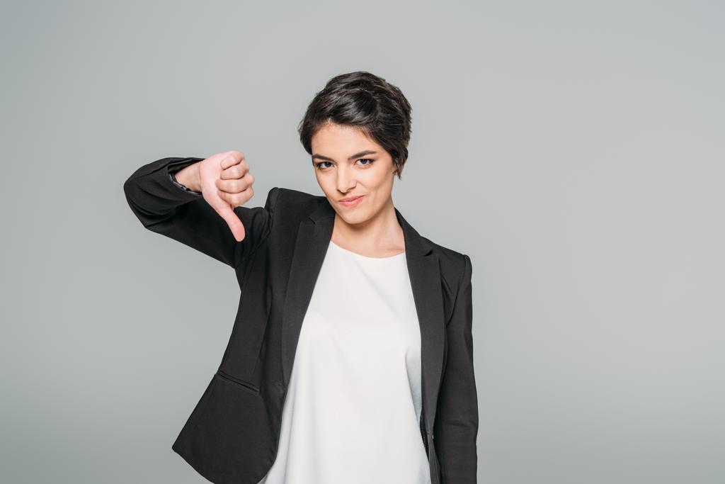 displeased mixed race businesswoman showing thumb down while looking at camera isolated on grey - Photo, Image