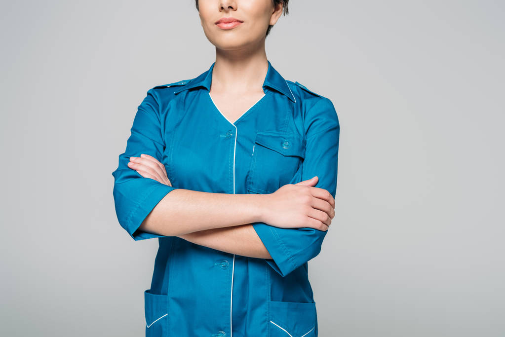 vista ritagliata di giovane infermiera razza mista in posa presso la fotocamera con le braccia incrociate isolato su grigio
 - Foto, immagini