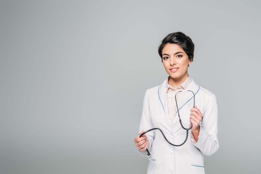 pretty mixed race doctor with stethoscope looking at camera isolated on grey - Photo, Image