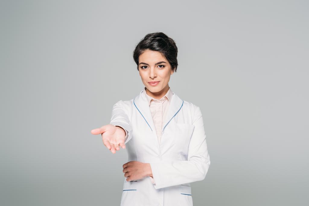 attractive mixed race doctor looking at camera with raised hand isolated on grey - Photo, Image