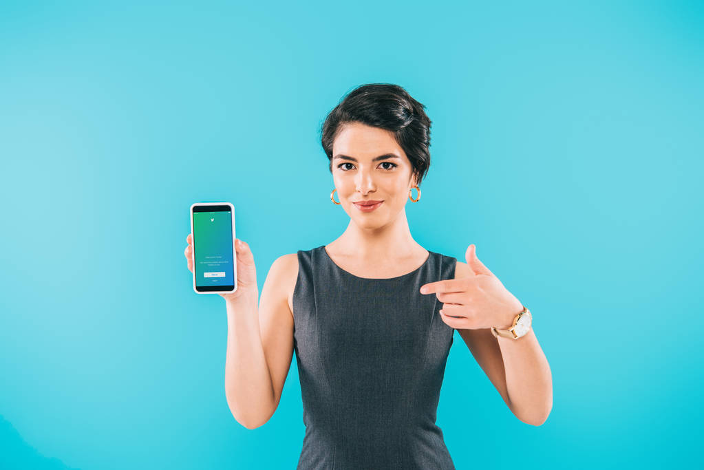 KYIV, UCRAINA - 24 APRILE 2019: Bella donna mista che punta il dito contro lo smartphone con l'app Twitter sullo schermo isolata sul blu
.  - Foto, immagini