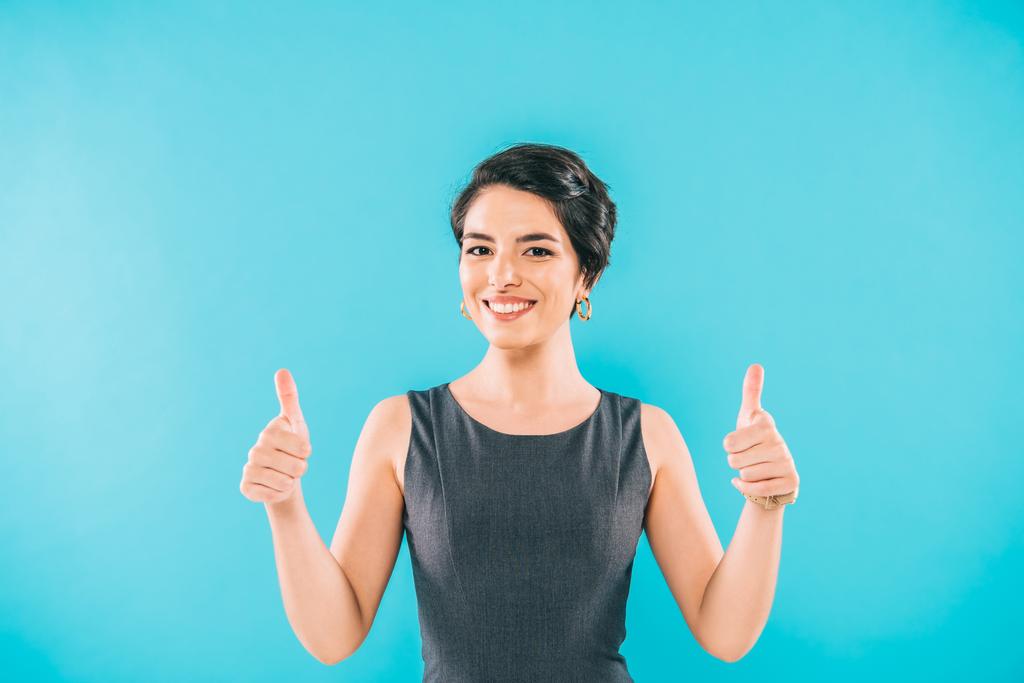 vrolijke mixed race vrouw met duimen omhoog en glimlachend op de camera geïsoleerd op blauw - Foto, afbeelding