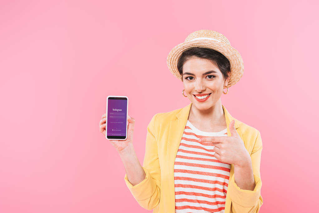キエフ、 ウクライナ - 2019年4月24日:ピンクで隔離された画面上のInstagramアプリでスマートフォンを示す笑顔の混合レース女性. - 写真・画像