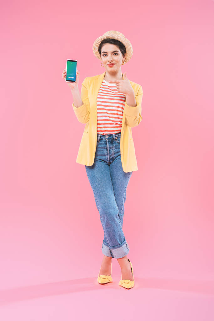 KYIV, UKRAINE - APRIL 24, 2019: Pretty mixed race woman showing smartphone with Twitter app on screen on pink background. - Photo, Image