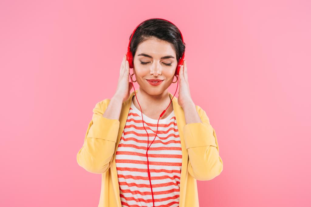 мрійлива змішана раса жінка слухає музику в навушниках із закритими очима ізольована на рожевому
 - Фото, зображення