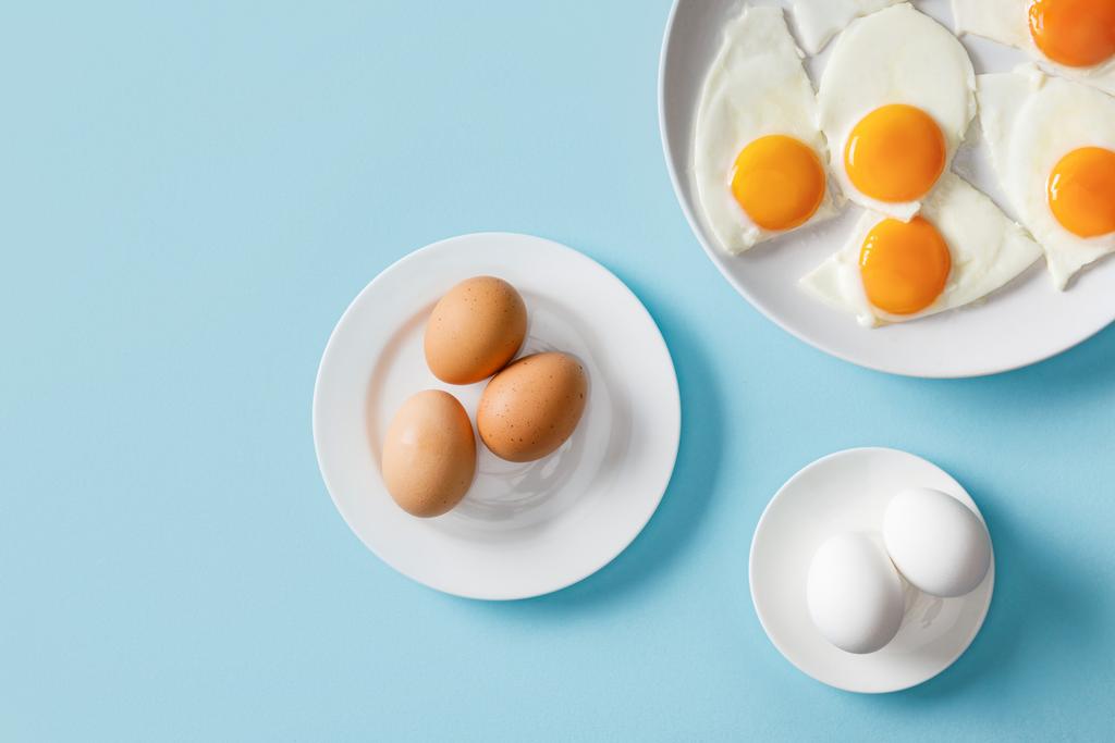 top view of fresh boiled and fried eggs on white plates on blue background - Photo, Image
