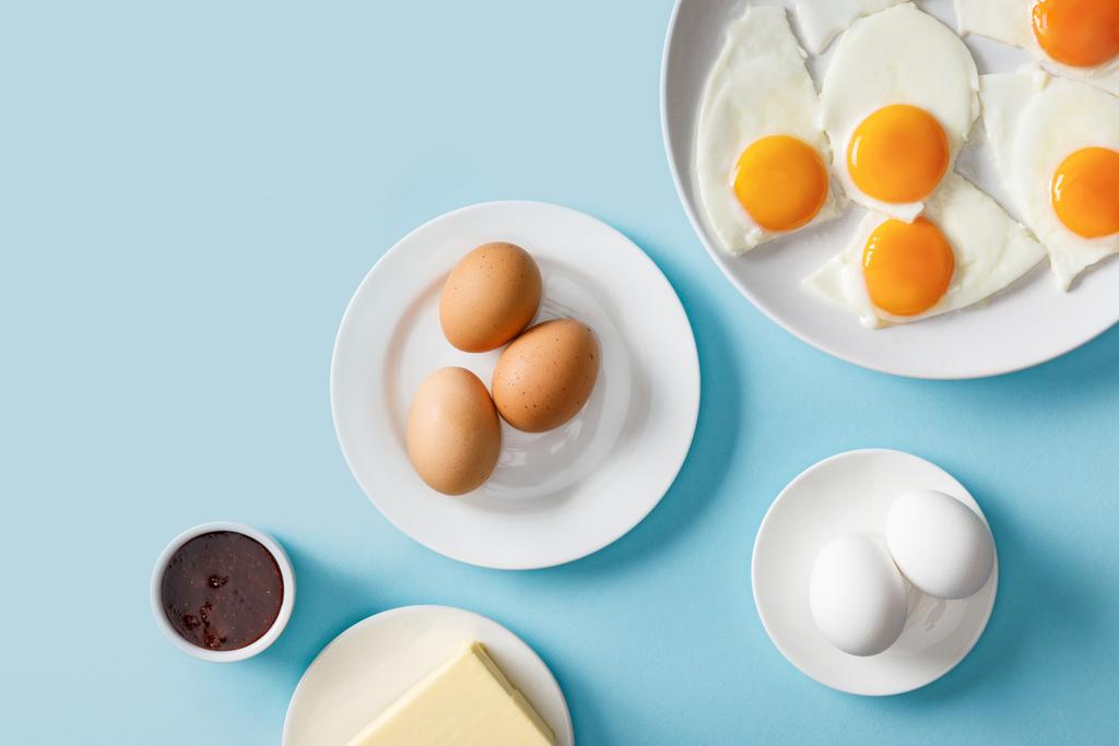 vista superior de huevos cocidos y fritos, mermelada y mantequilla sobre fondo azul
 - Foto, Imagen