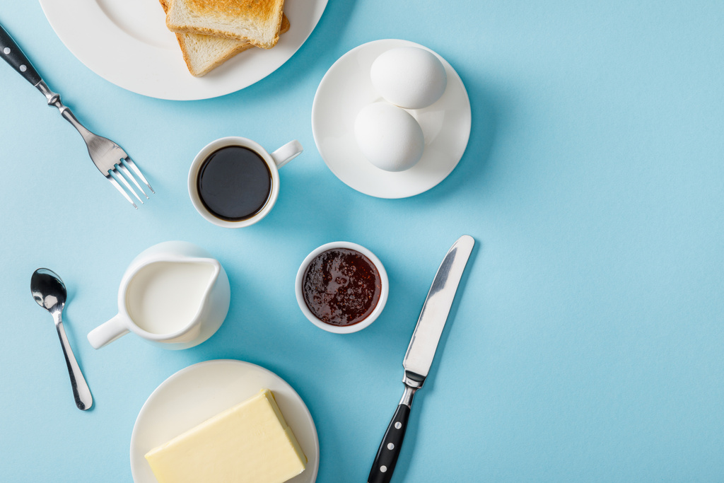 vista dall'alto di uova fresche, marmellata, caffè, posate, burro e due brindisi su piatti bianchi su sfondo blu
 - Foto, immagini