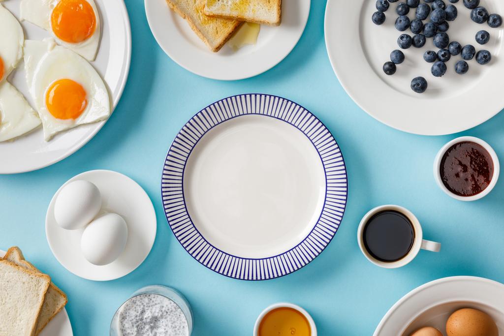 Draufsicht auf das servierte Frühstück mit leerem Teller in der Mitte auf blauem Hintergrund - Foto, Bild