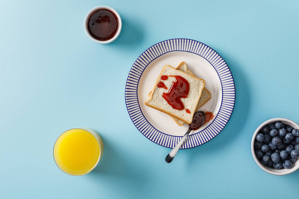 vista superior de zumo de naranja, arándanos, tostadas, tazón y cuchara con mermelada en el plato sobre fondo azul
 - Foto, Imagen