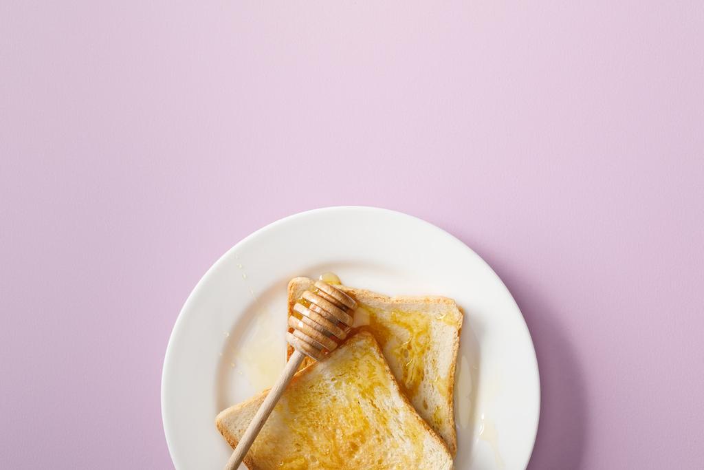 top view of toasts with honey and wooden dipper on white plate on violet background - Photo, Image