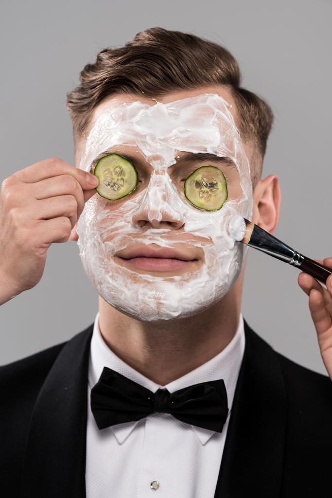 partial view of cosmetologists applying cucumber mask and man in formal wear isolated on grey - Photo, Image