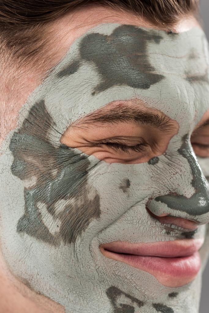 Close-up weergave van lachende jonge man met klei masker met gesloten ogen - Foto, afbeelding