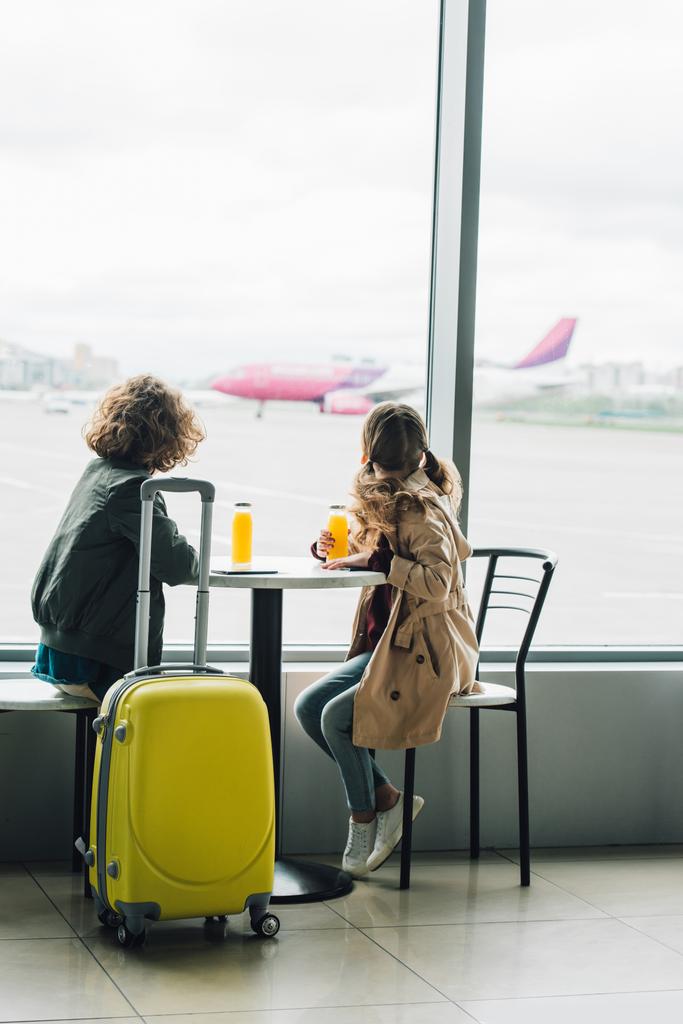 Kinder sitzen mit Saft am Tisch neben gelbem Koffer und schauen im Flugzeug aus dem Fenster - Foto, Bild