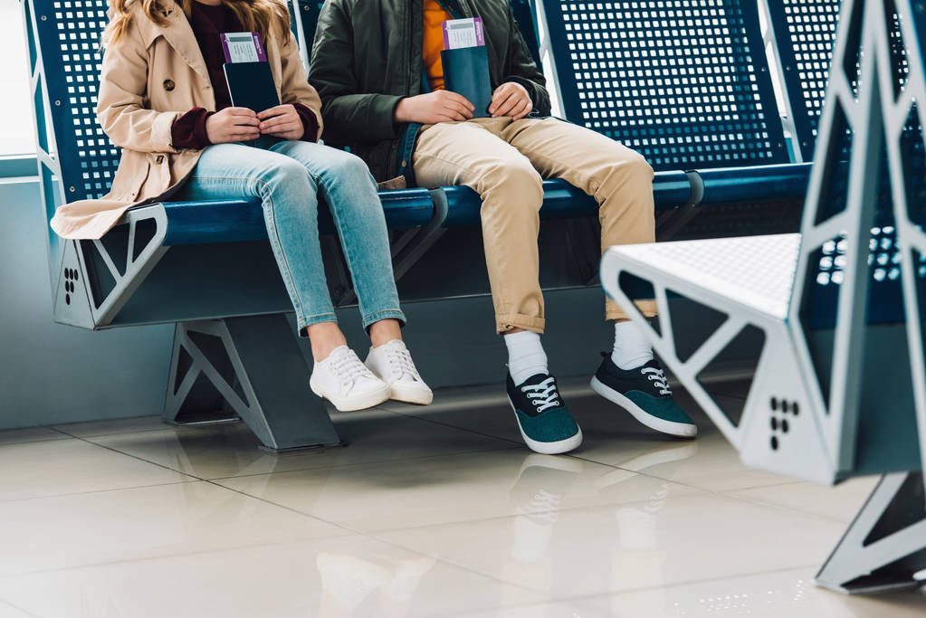 wykadrowany widok dzieci siedzących na niebieskich krzeseł i trzymających paszporty w poczekalni na lotnisku - Zdjęcie, obraz