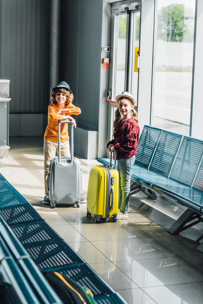 прелестные дети-подростки с чемоданами в зале ожидания, смотрящие в камеру
 - Фото, изображение