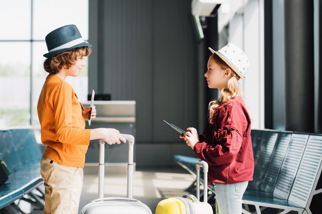 Προεφηβικό παιδιά με βαλίτσες, αεροπορικά εισιτήρια και διαβατήρια στην αίθουσα αναμονής - Φωτογραφία, εικόνα