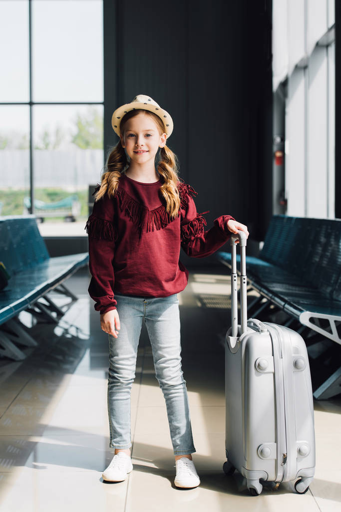 uśmiechnięty preteen dziecko z walizka w poczekalni w porcie lotniczym - Zdjęcie, obraz