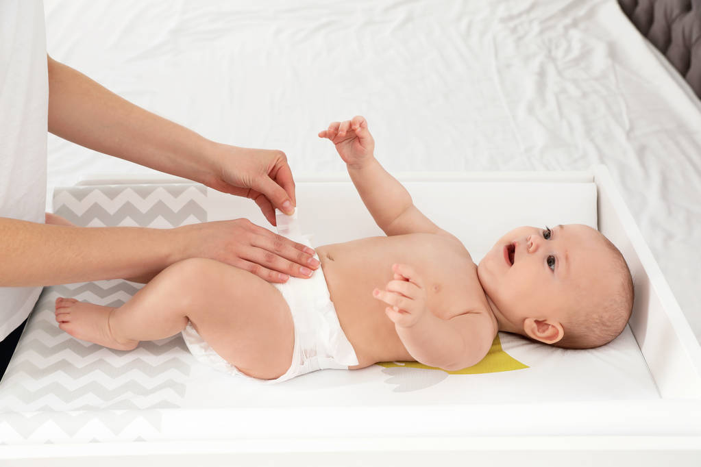 Mother changing her baby's diaper on table indoors - Photo, Image