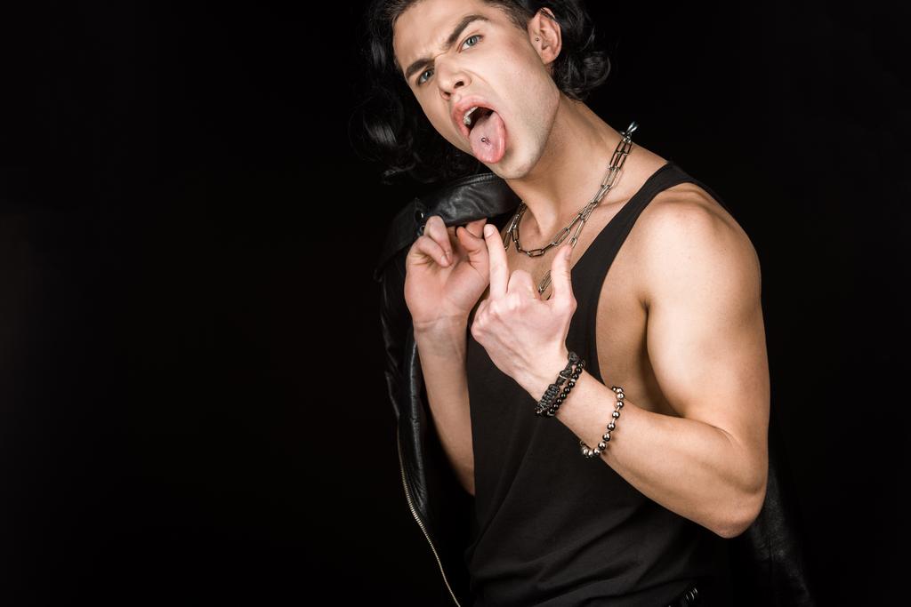 mladý muž ukazující prostředníček a jazyk při držení kožené bundy izolované na černé  - Fotografie, Obrázek