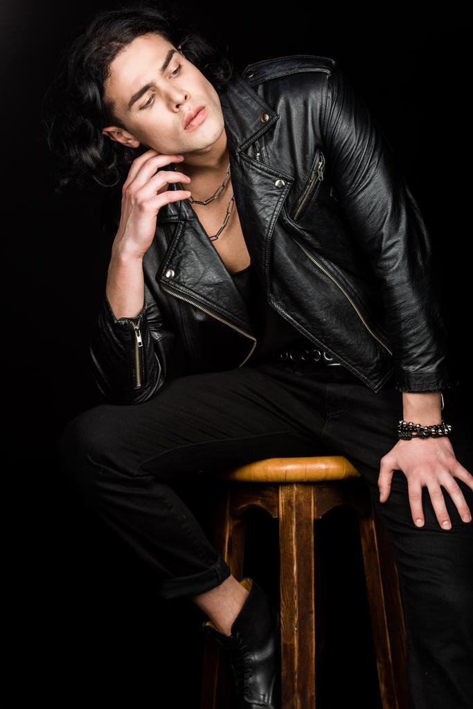 pensive man in leather jacket sitting on chair isolated on black  - Photo, Image