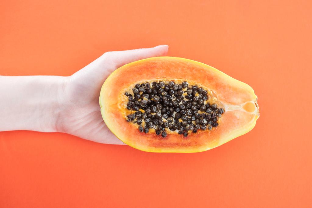 vista recortada de la mujer sosteniendo madura mitad papaya exótica con semillas negras aisladas en naranja
 - Foto, Imagen