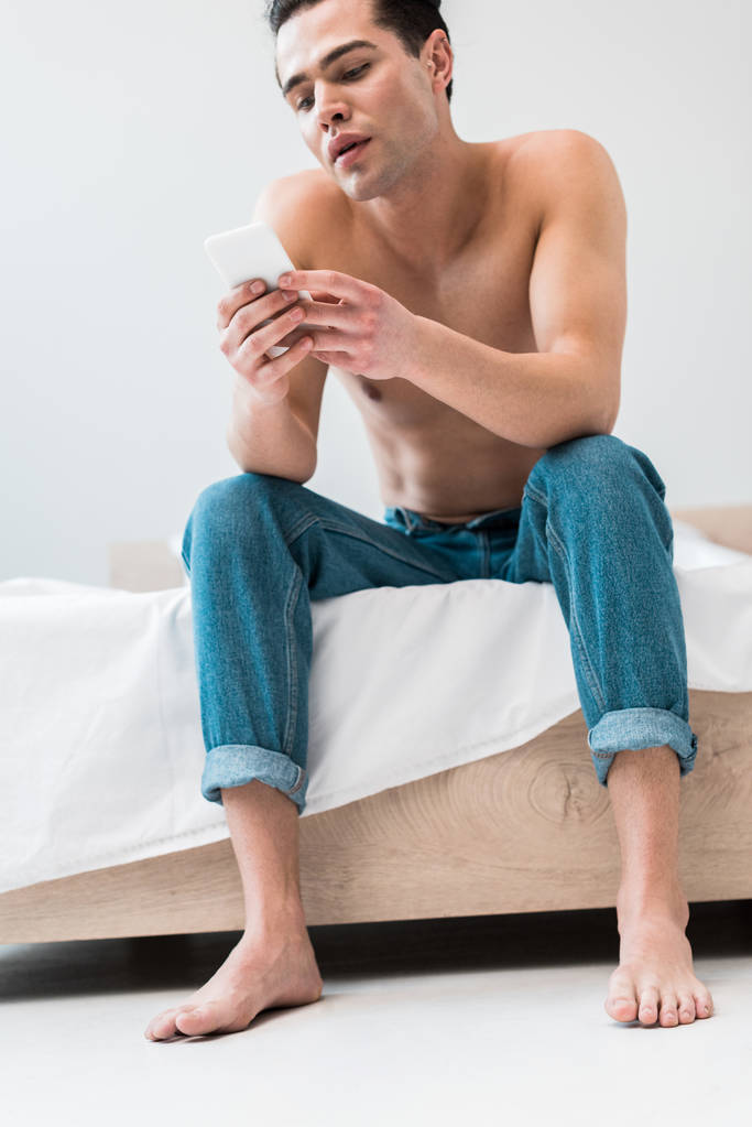 niski kąt widzenia człowieka siedzącego na łóżku i za pomocą smartfona  - Zdjęcie, obraz