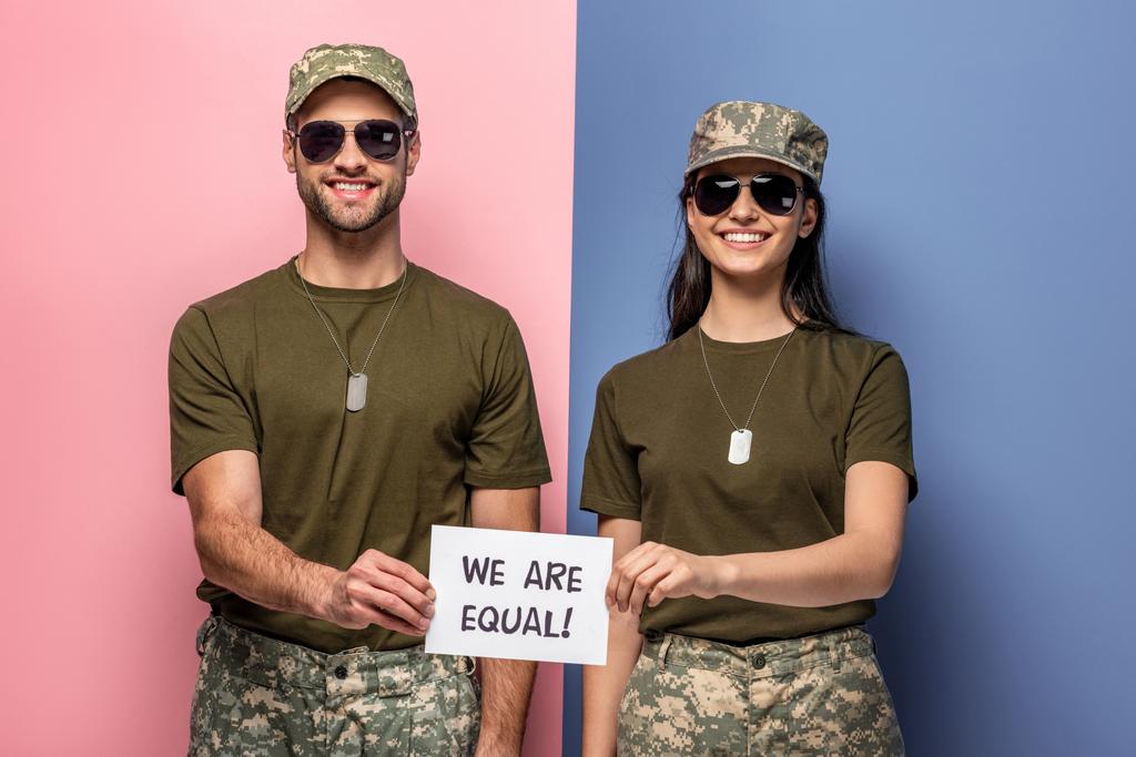 šťastný muž a žena ve vojenském uniformním držení papíru jsme si rovni! nápisy na modré a růžové - Fotografie, Obrázek