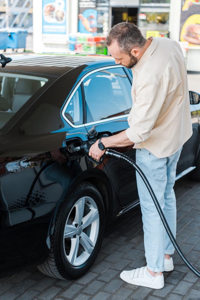 hombre barbudo repostando coche negro mientras está de pie en la gasolinera
  - Foto, imagen