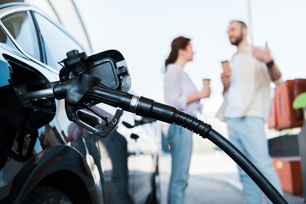 επιλεκτική εστίαση του ανεφοδιασμού μαύρων αυτοκινήτων με βενζίνη κοντά σε άνθρωπο και γυναίκα στο βενζινάδικο  - Φωτογραφία, εικόνα