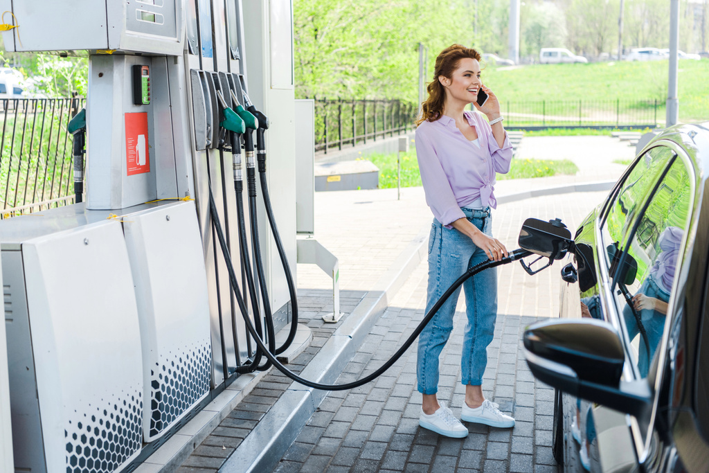 iloinen nainen tilalla polttoainepumppu tankkauksen auton bentsiini ja puhuu älypuhelimella
  - Valokuva, kuva