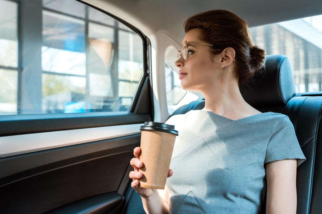arabada otururken kağıt bardak tutan gözlüklü kadının düşük açılı görünümü  - Fotoğraf, Görsel