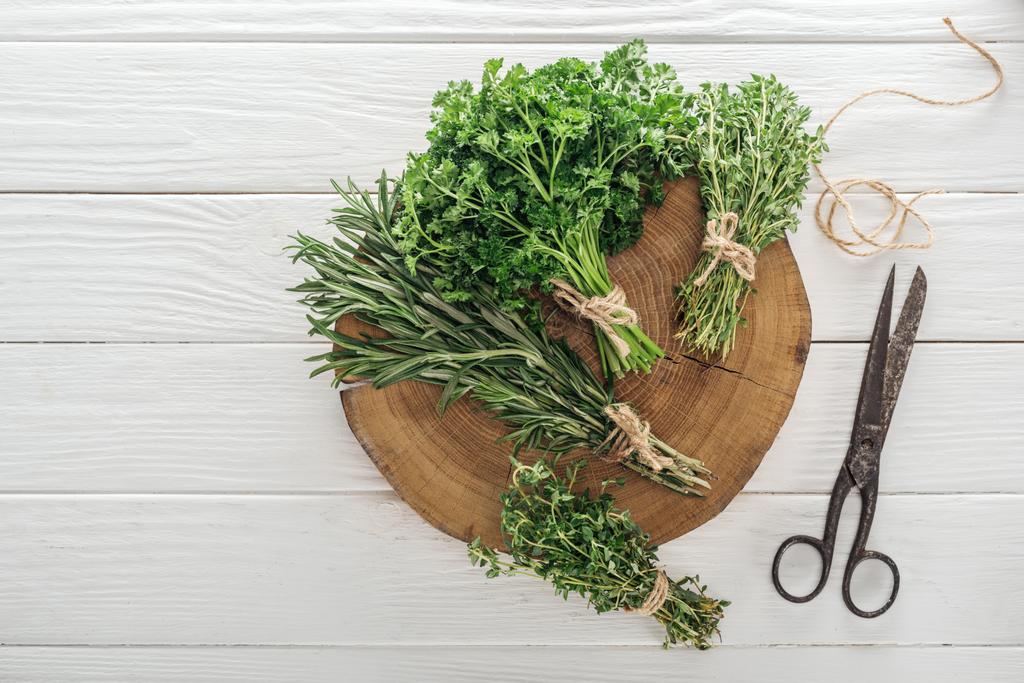 top view of green parsley, rosemary and thyme on brown stump near vintage scissors on white wooden table - Photo, Image