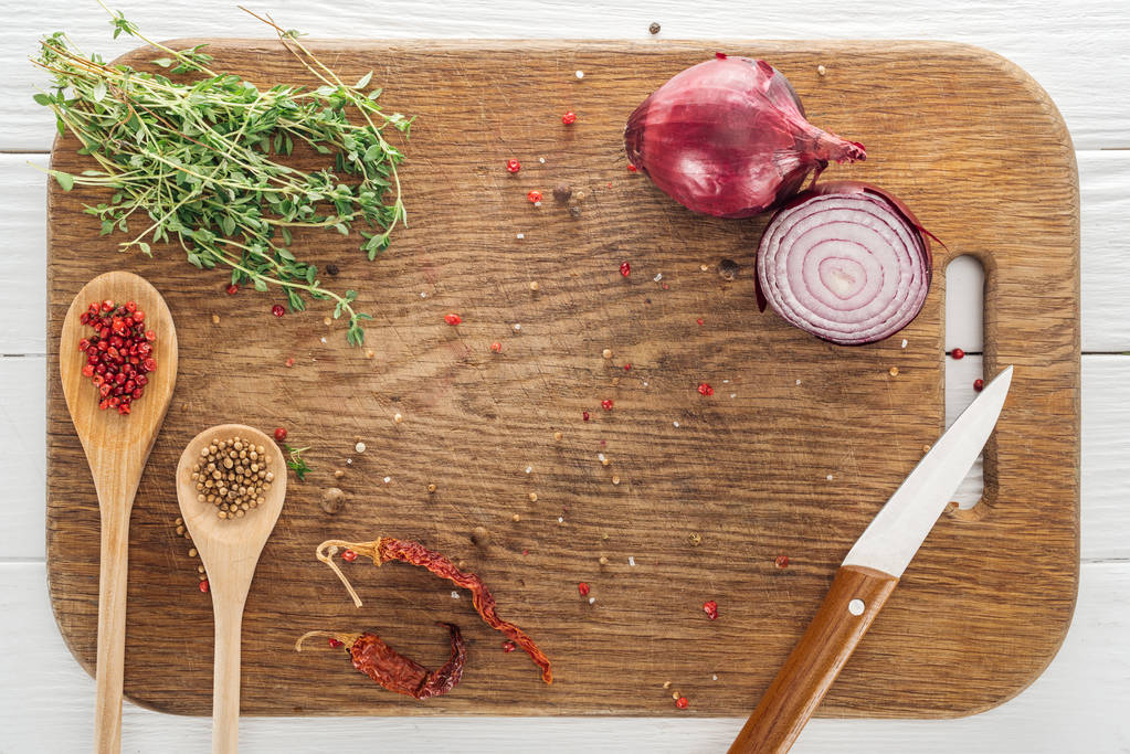 top view of thyme, knife, spoons with coriander and pink peppercorn, dried chili peppers and red onion on wooden chopping board - Photo, Image