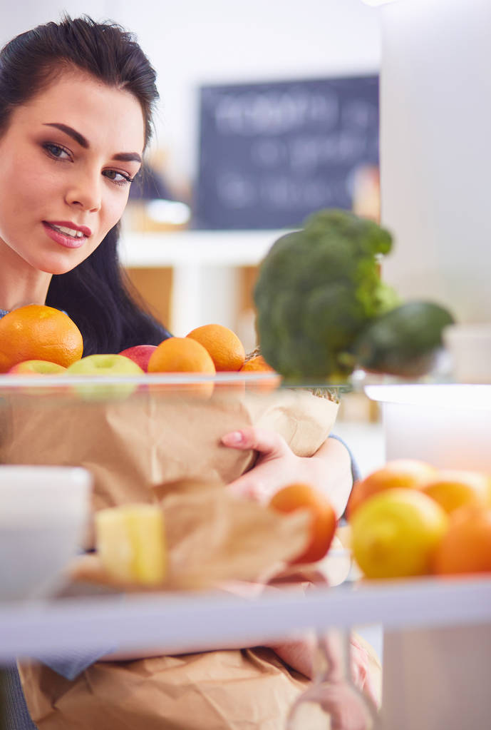 Gülümseyen kadın buzdolabından taze meyve alıyor, sağlıklı yiyecek konsepti. - Fotoğraf, Görsel